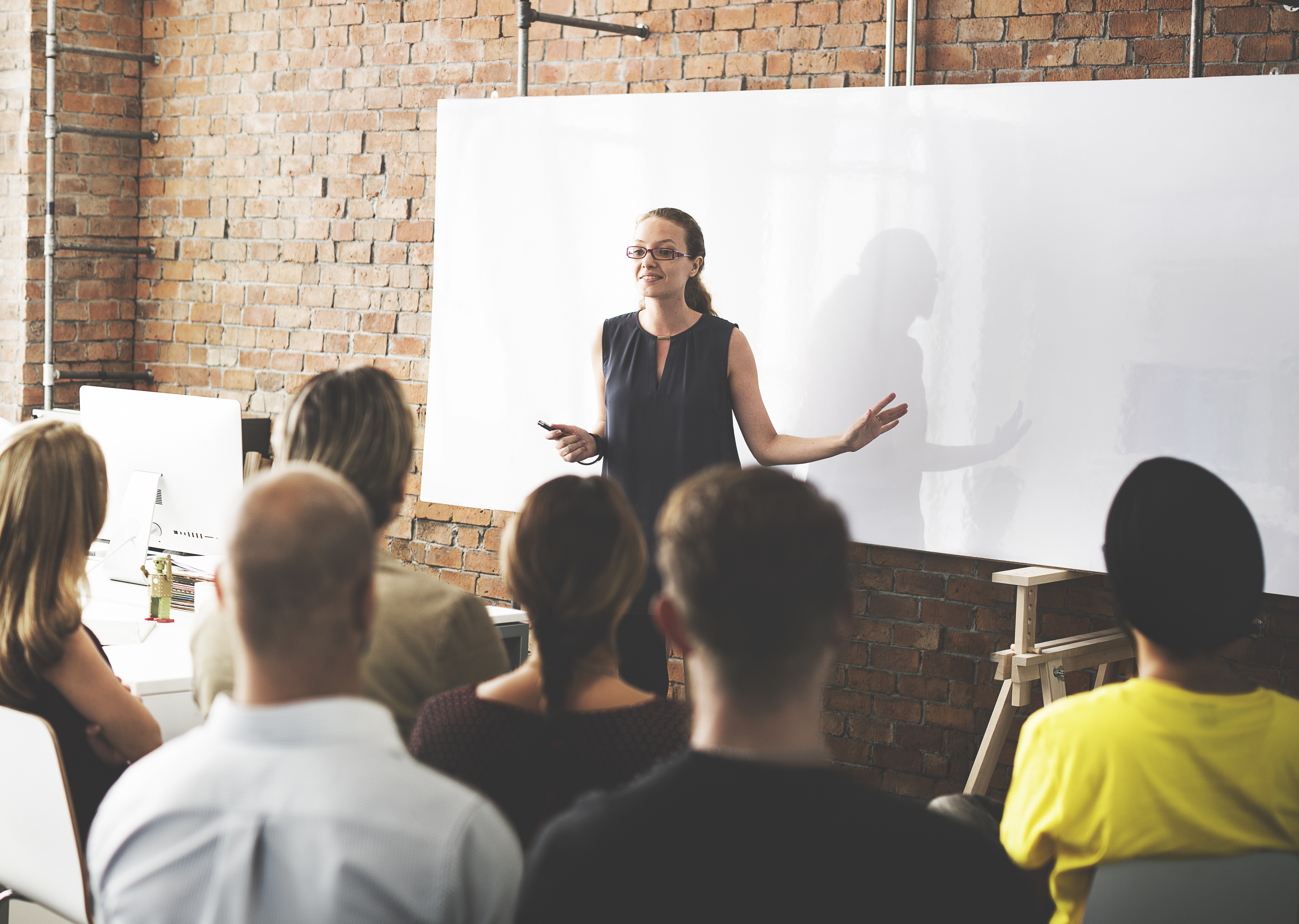 A Woman in front of a whiteboard facilitating a professional learning session to a group of people