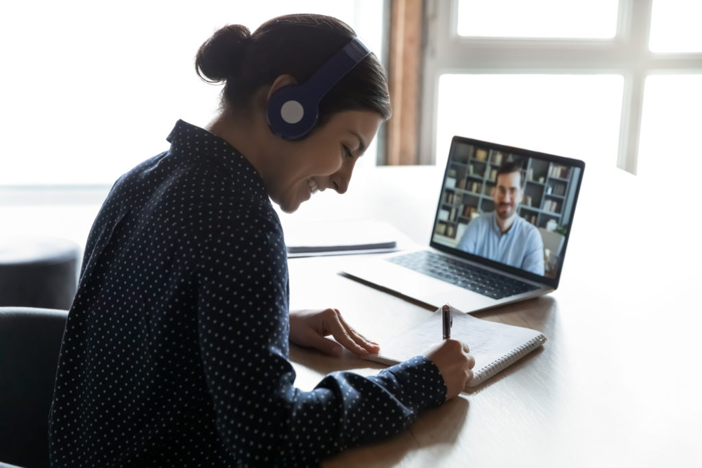 A woman on a virtual call with headphone on while writing in her book