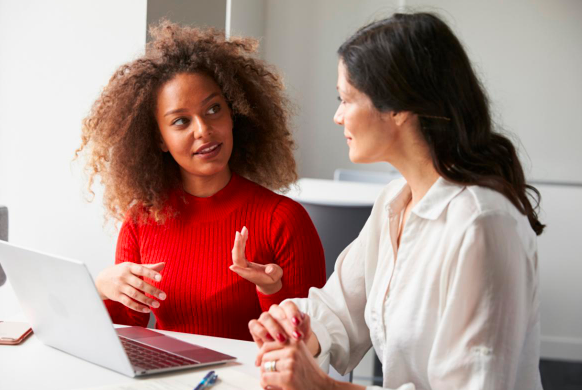 two adults sitting at the table with their laptop open talking to one another