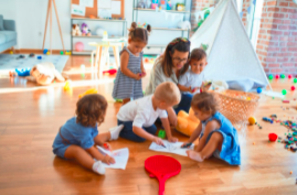 An educator and 5 children in the classroom on the floor colouring