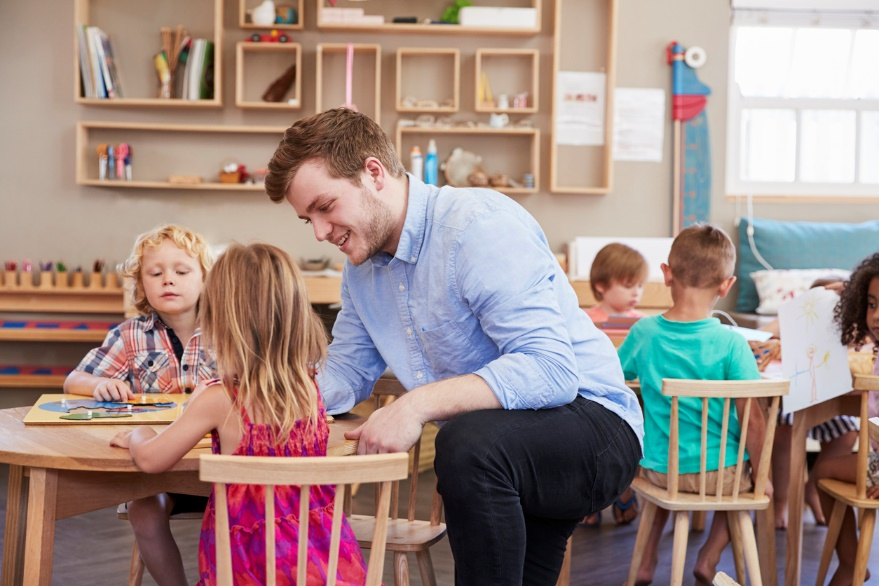 An educator bending down at the table with two children sitting on the chair