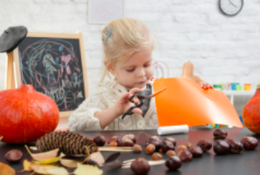 A child sitting at the craft table using scissors to cut orange construction papers