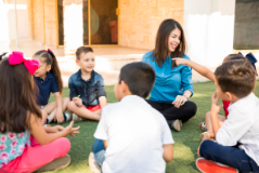 adult and 7 children sitting in a circle outside on the grass